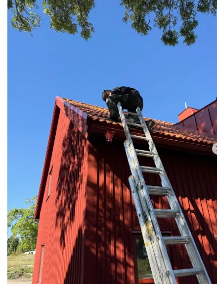 Tekniker på taket till ett rött hus vid skorstensarbete